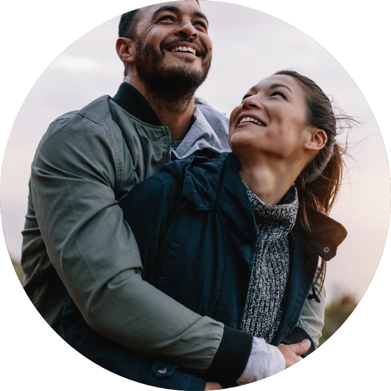 A man hugs a woman from behind while both of them smile.