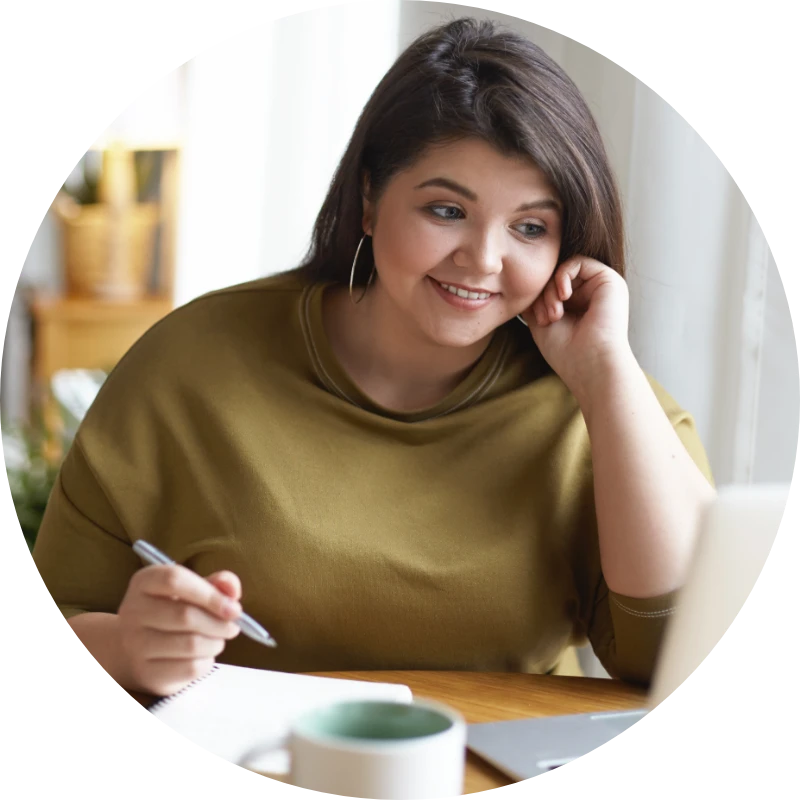 A young woman with a pen in her hand looks at her laptop.