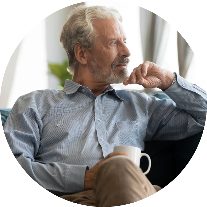 An older man looks out the window while holding a coffee mug.